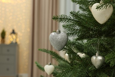 Photo of Beautiful baubles in shape of hearts hanging on Christmas tree indoors. Space for text