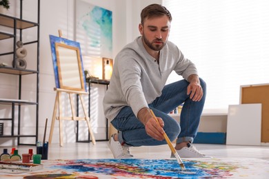 Photo of Young man painting on canvas with brush in artist studio