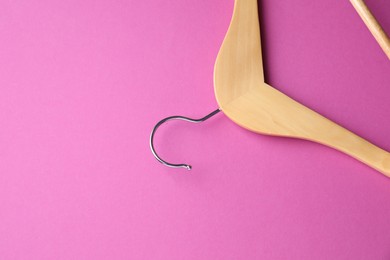 Photo of Empty wooden hanger on bright pink background, top view. Space for text
