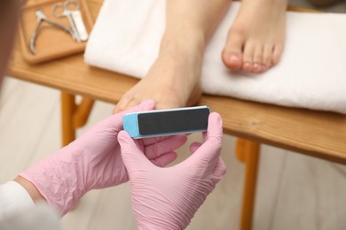 Professional pedicurist filing client`s toenails in beauty salon, closeup