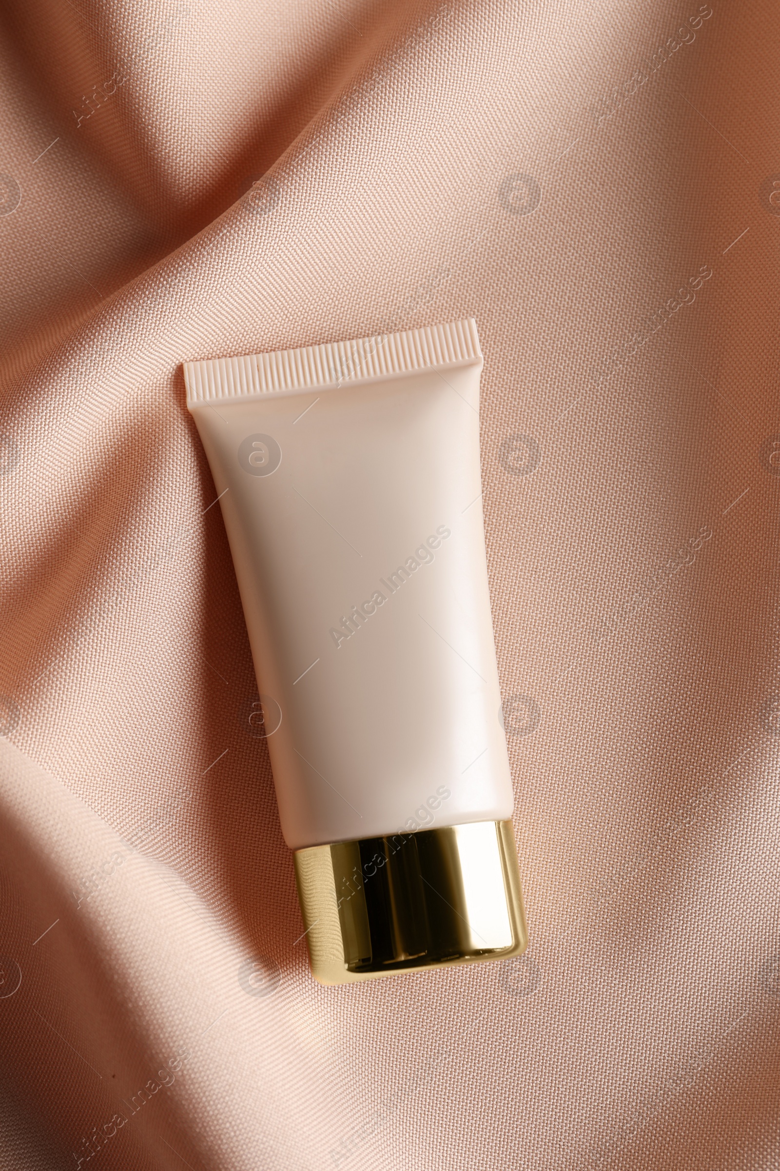 Photo of Tube of skin foundation on beige cloth, top view. Makeup product