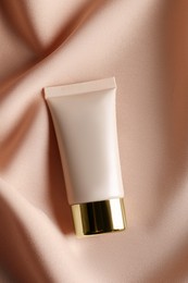 Tube of skin foundation on beige cloth, top view. Makeup product