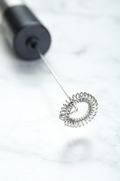 Photo of Black milk frother wand on white marble table, closeup