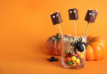 Photo of Delicious candies decorated as monsters on orange background, space for text. Halloween treat