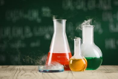 Laboratory glassware with colorful liquids on wooden table, space for text. Chemical reaction