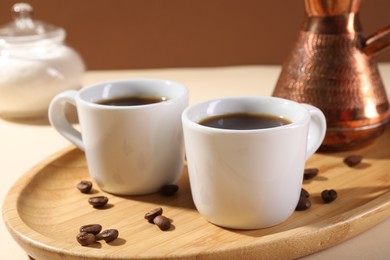 Photo of Delicious coffee in cups and beans on beige table, closeup