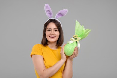 Easter celebration. Happy woman with bunny ears and wrapped egg on grey background