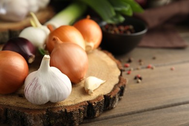 Photo of Fresh onion bulbs, leek and garlic on wooden table, closeup. Space for text