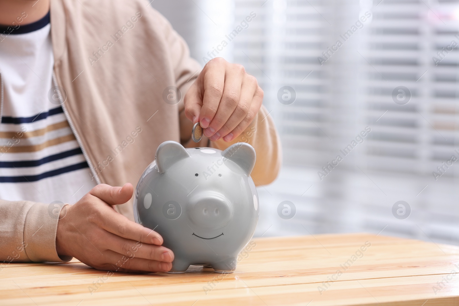 Photo of Man putting coin into piggy bank at wooden table, closeup. Space for text