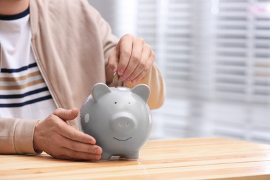 Photo of Man putting coin into piggy bank at wooden table, closeup. Space for text