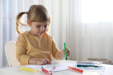 Photo of Cute little girl drawing with marker at white table indoors. Child`s art