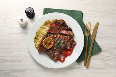 Photo of Delicious grilled beef steak and vegetables served on light wooden table, top view