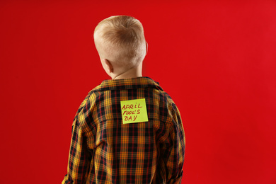 Photo of Little boy with APRIL FOOL'S DAY sticker on back against red background