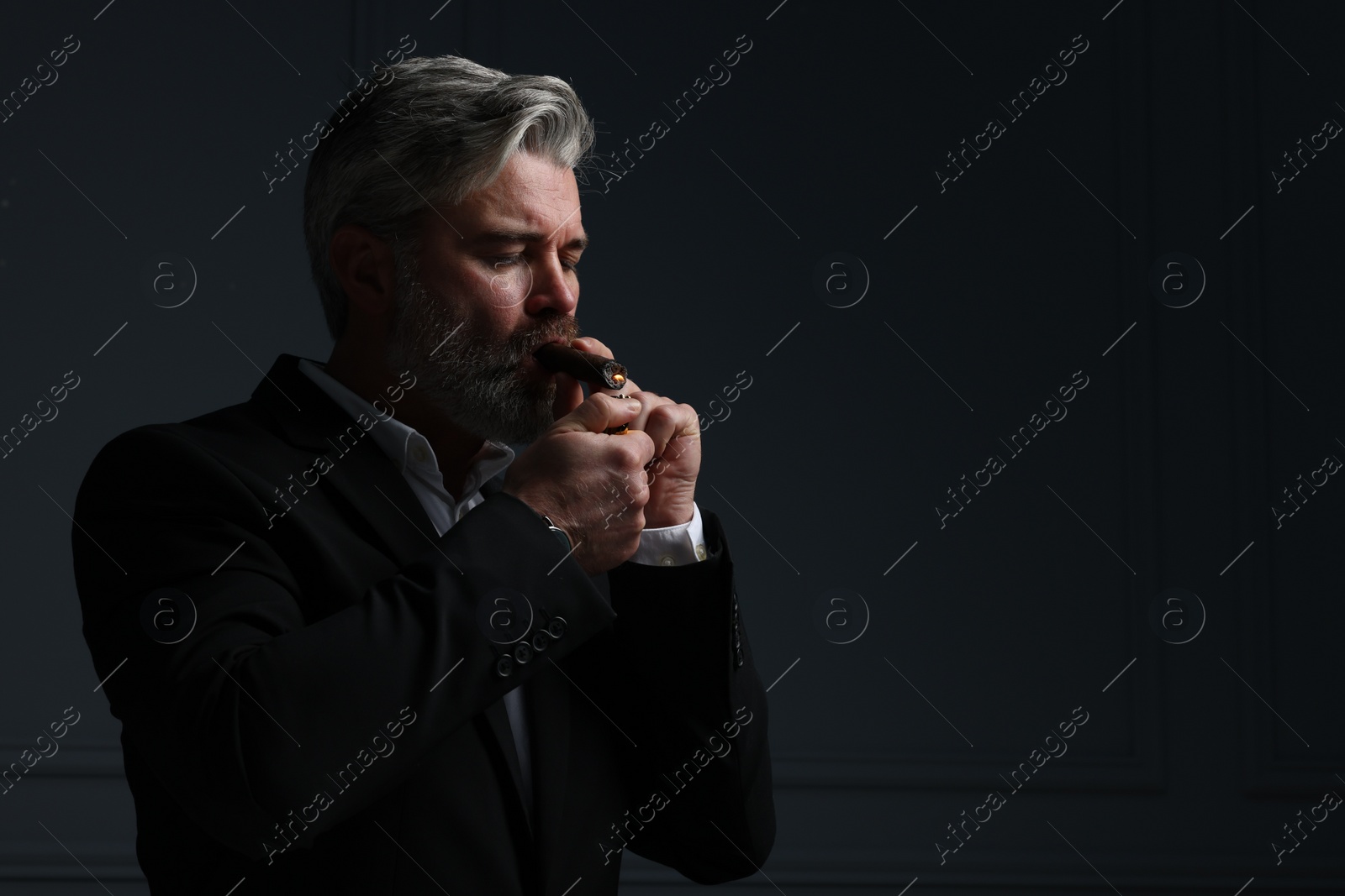 Photo of Bearded man lighting cigar on dark grey background. Space for text