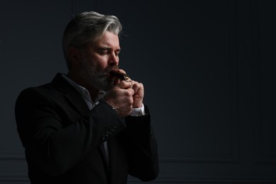 Photo of Bearded man lighting cigar on dark grey background. Space for text