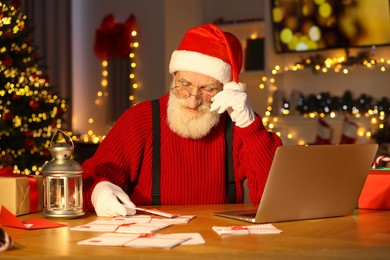 Santa Claus reading letter at his workplace in room decorated for Christmas