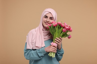 Happy woman in hijab with beautiful bouquet on beige background