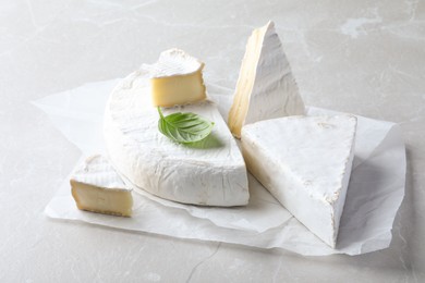 Photo of Delicious brie cheese with basil on light grey table
