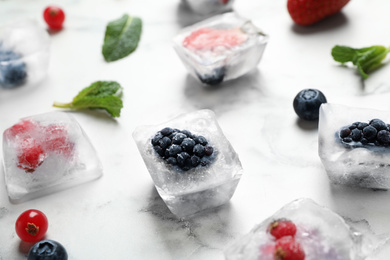 Photo of Ice cubes with different berries and mint on white marble table, closeup
