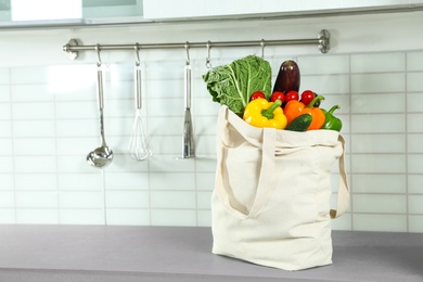Photo of Textile shopping bag full of vegetables on countertop in kitchen. Space for text