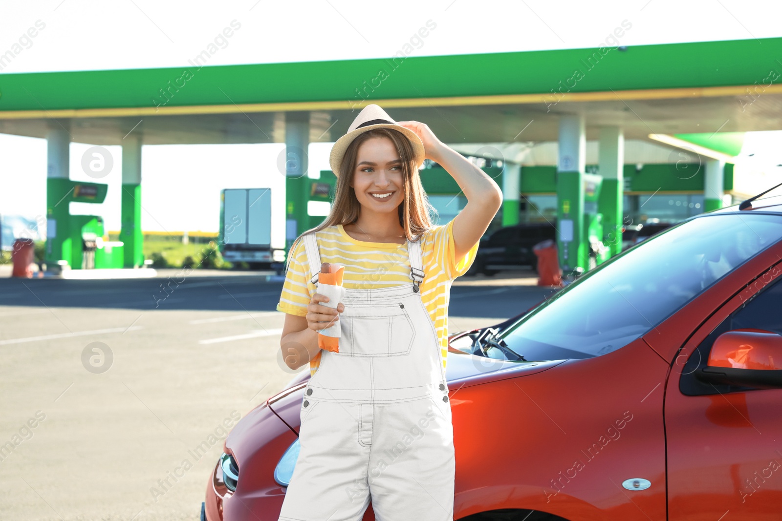 Photo of Beautiful young woman with hot dog near car at gas station