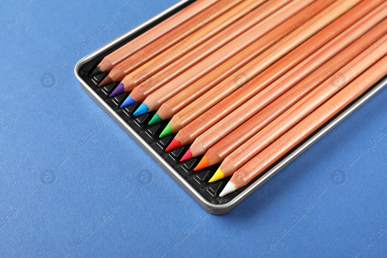 Photo of Box with many colorful pastel pencils on blue background, closeup. Drawing supplies