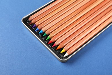 Box with many colorful pastel pencils on blue background, closeup. Drawing supplies