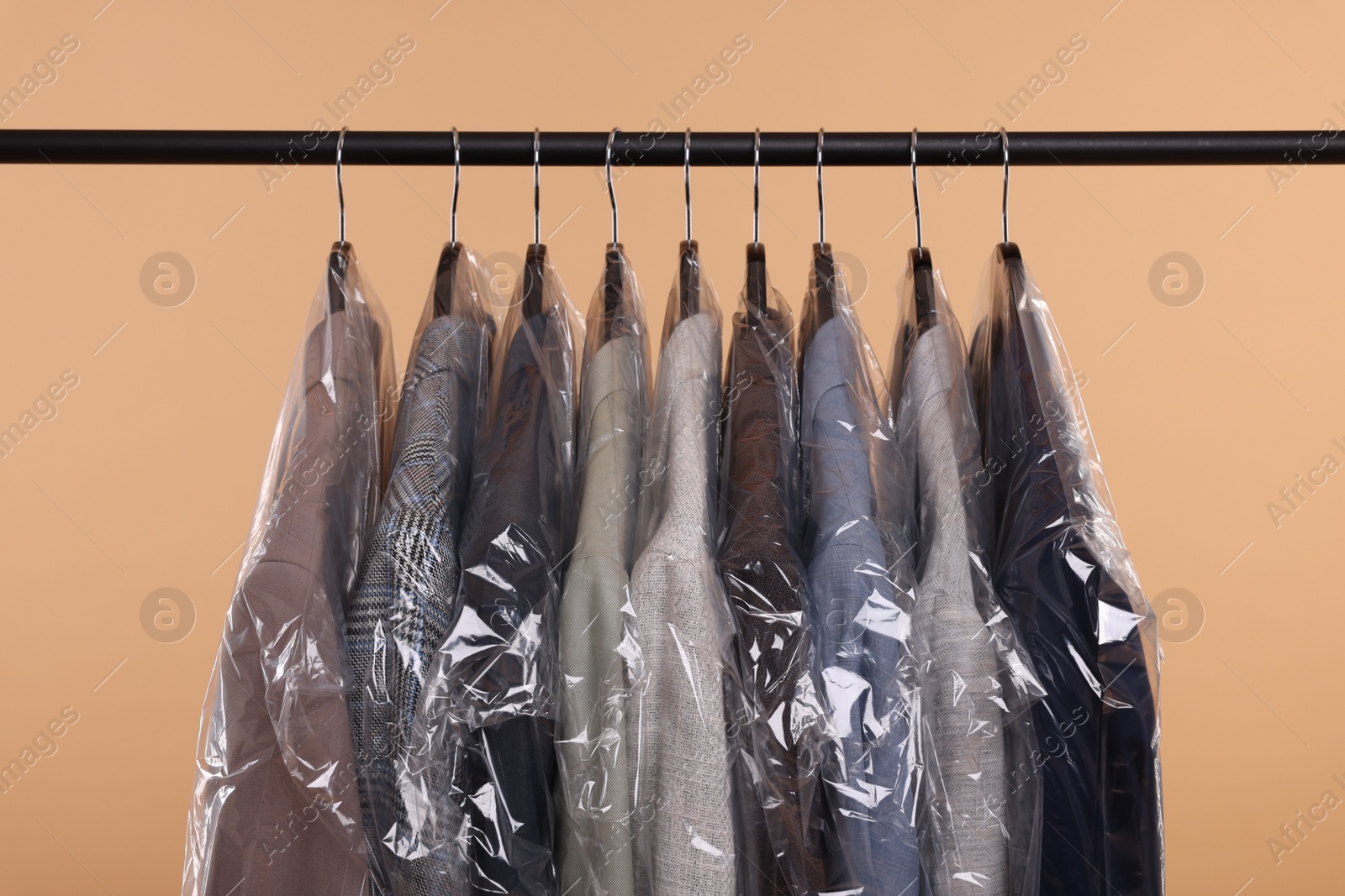 Photo of Dry-cleaning service. Many different clothes in plastic bags hanging on rack against beige background