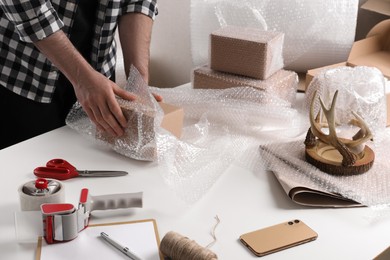 Photo of Man covering box with bubble wrap at table in warehouse, closeup