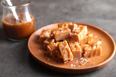 Photo of Plate with tasty candies, caramel sauce and salt on grey table, closeup