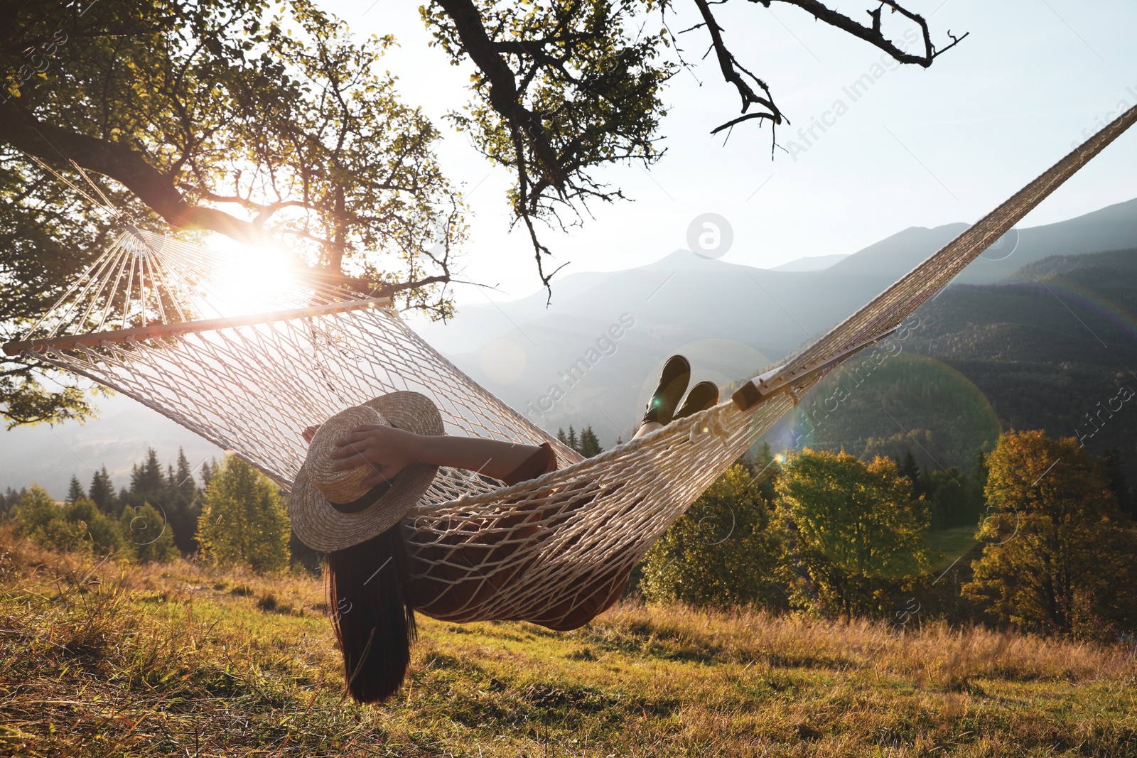 Photo of Young woman resting in hammock outdoors at sunset