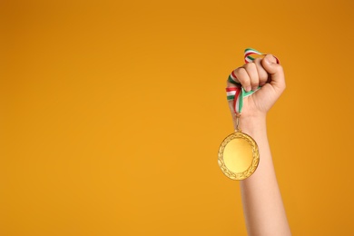 Photo of Woman holding gold medal on yellow background, closeup. Space for text