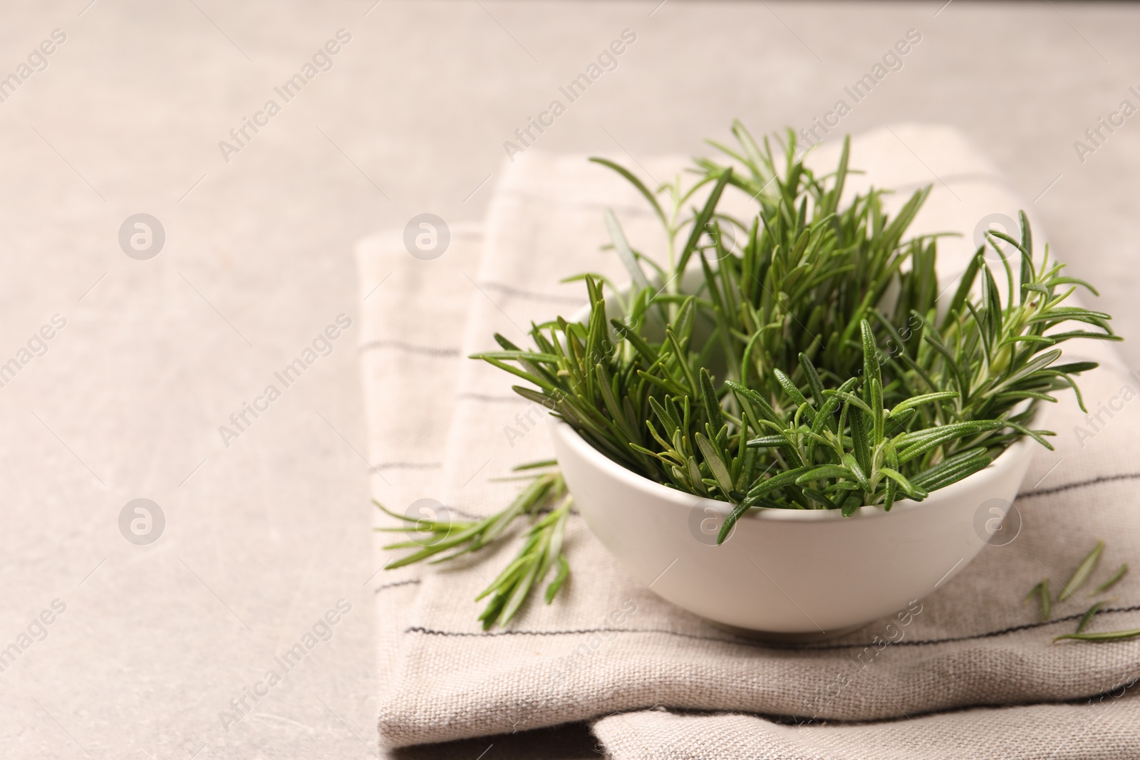 Photo of Bowl with fresh green rosemary on light grey table, space for text