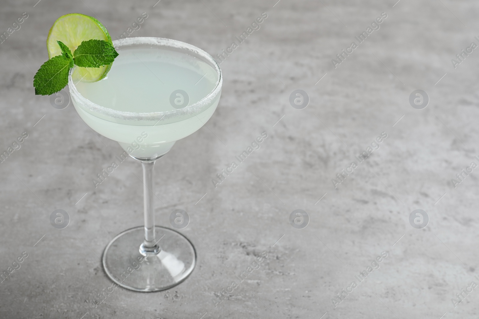 Photo of Glass of tasty refreshing cocktail with mint and lime on grey table. Space for text