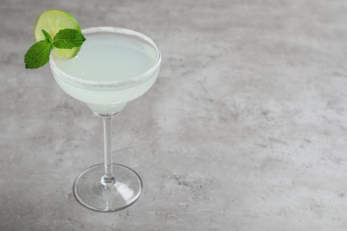 Photo of Glass of tasty refreshing cocktail with mint and lime on grey table. Space for text