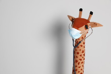 Toy giraffe with face mask and stethoscope on white background, space for text. Pediatrician practice