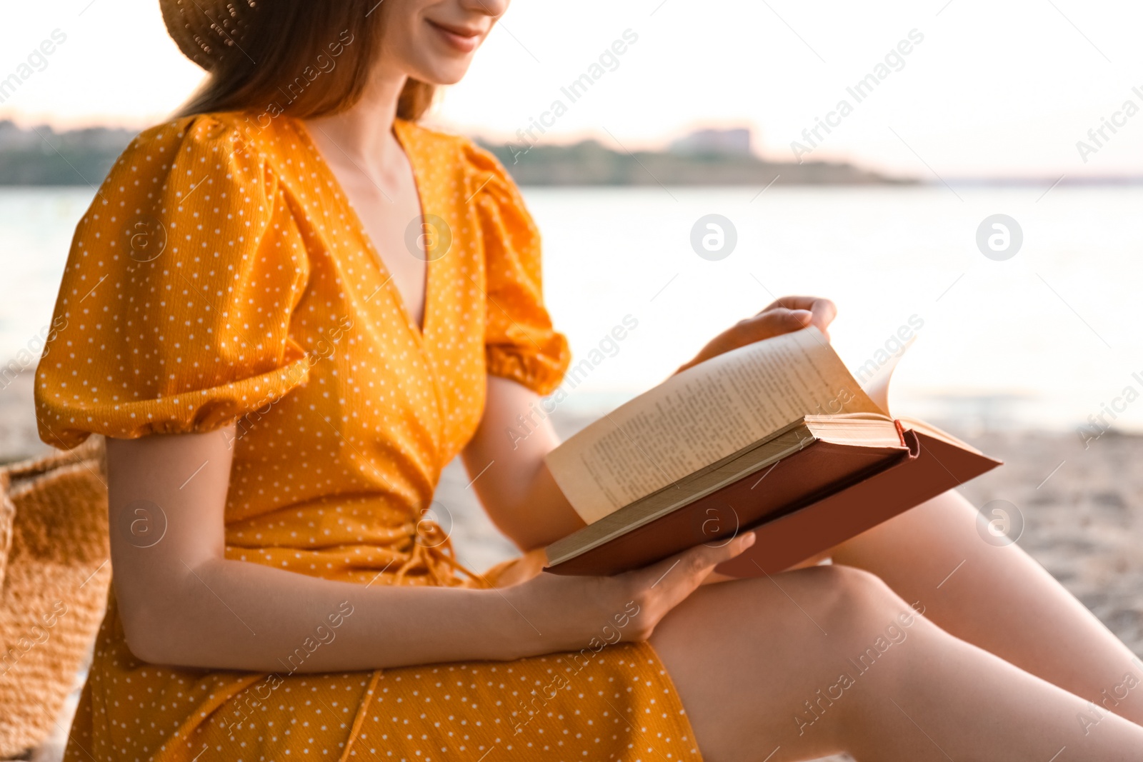 Photo of Young woman reading book on sandy beach near sea, closeup