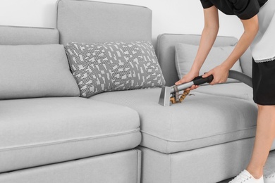 Photo of Female worker removing dirt from sofa with professional vacuum cleaner indoors