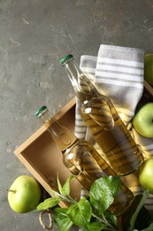Delicious cider, ripe apples and green leaves on gray table, flat lay