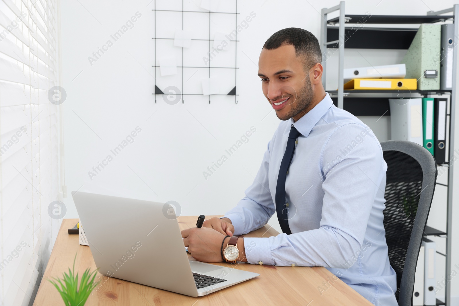 Photo of Happy young intern working with laptop at table in modern office