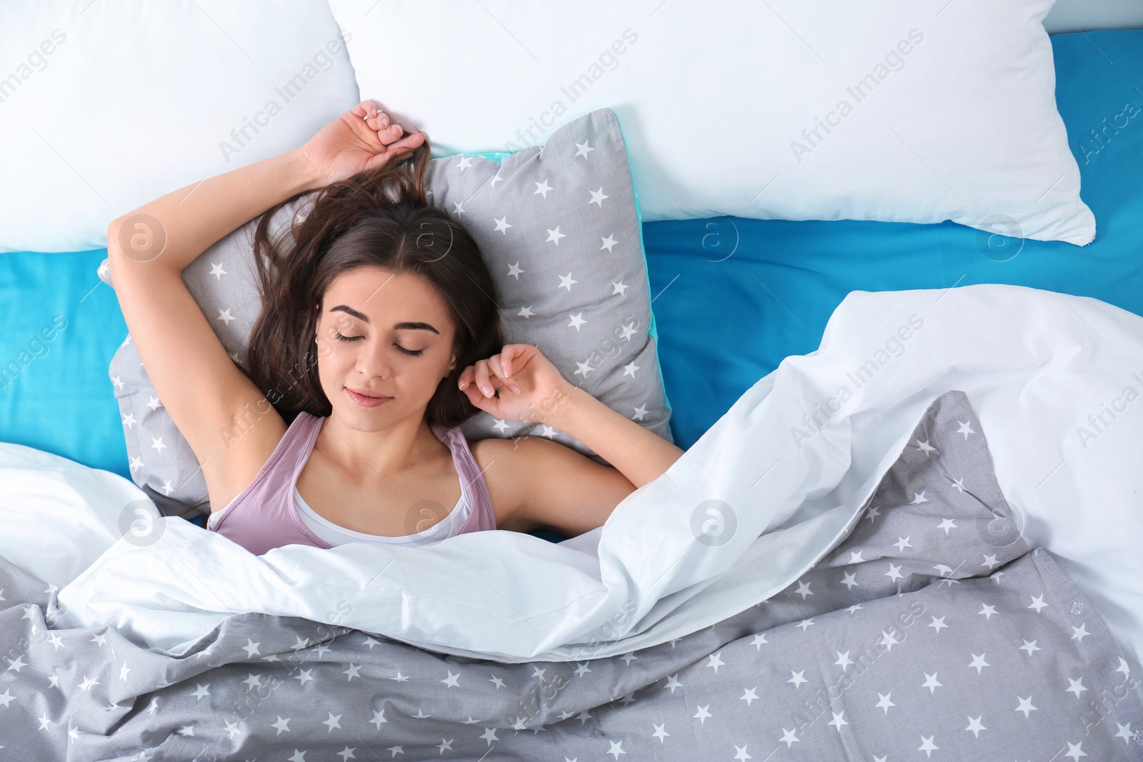 Photo of Young woman sleeping on soft pillow, top view. Bedtime