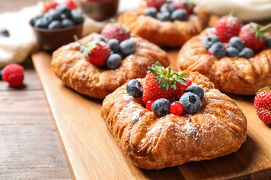 Fresh delicious puff pastry with sweet berries on wooden board, closeup