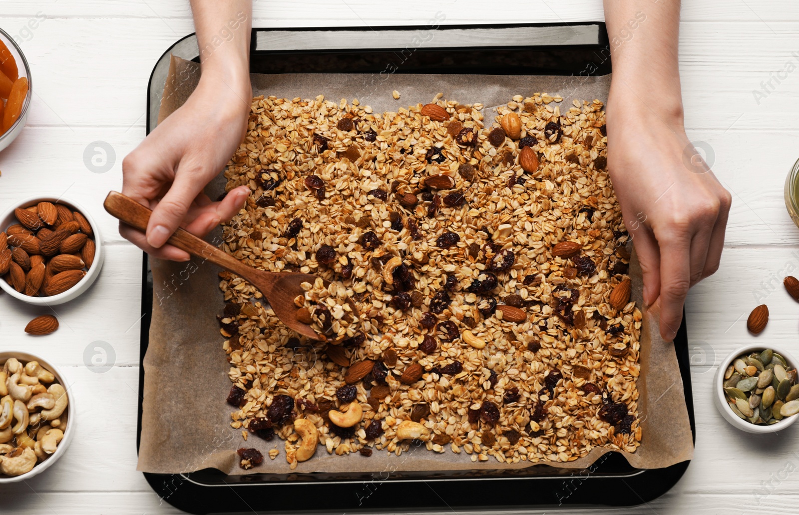 Photo of Woman taking tasty granola with spoon from tray at white wooden table, top view