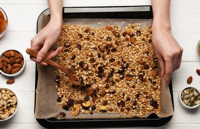 Photo of Woman taking tasty granola with spoon from tray at white wooden table, top view