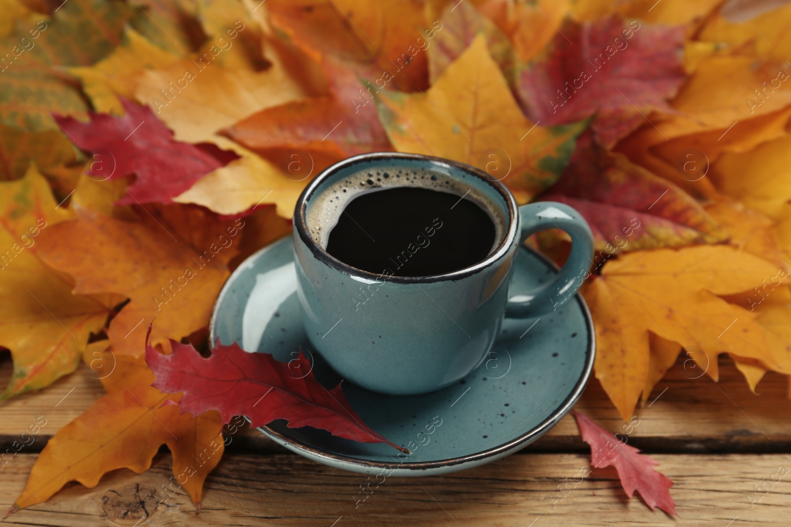 Photo of Cup of hot coffee and autumn leaves on wooden table