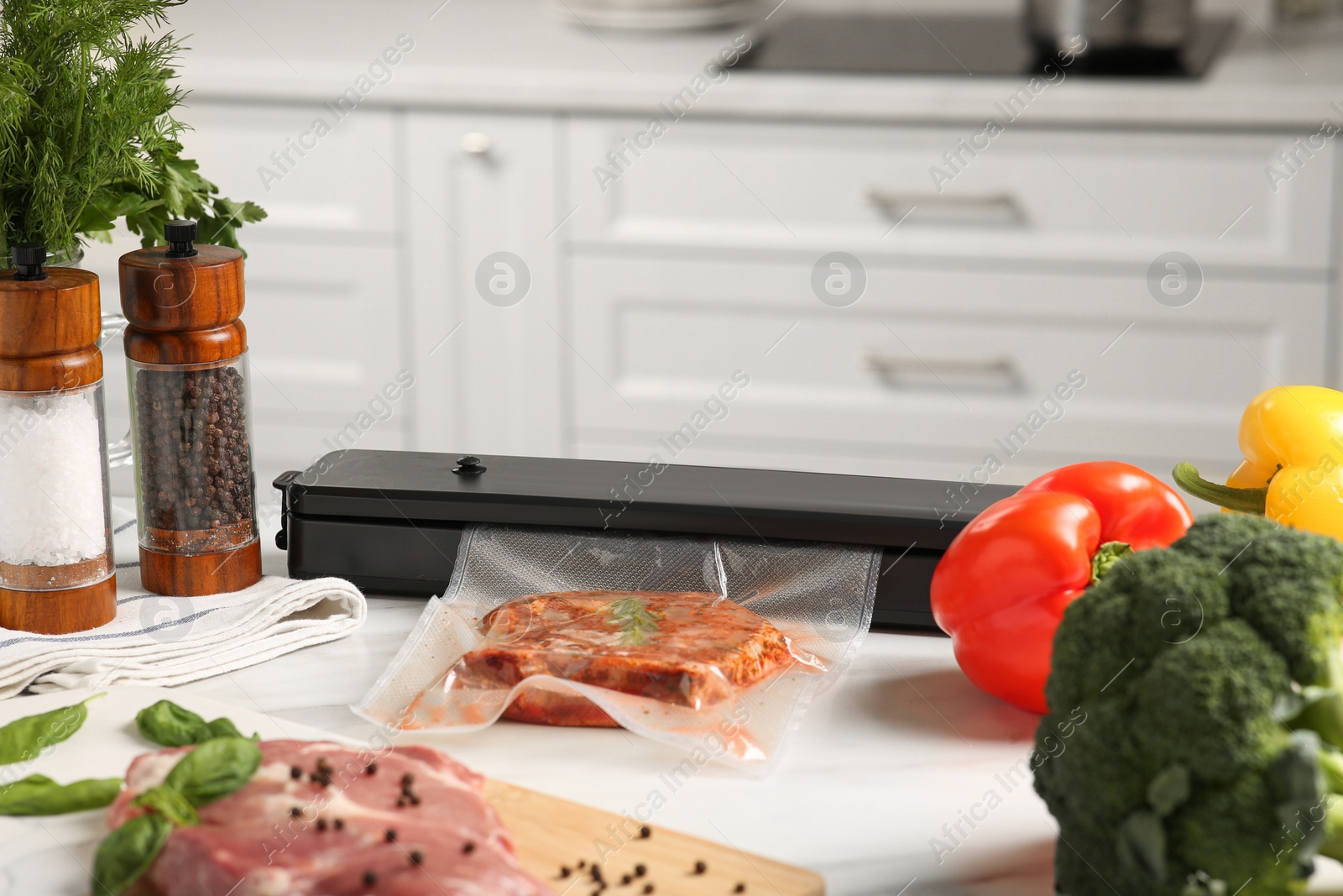 Photo of Sealer for vacuum packing with meat in plastic bag on white kitchen table