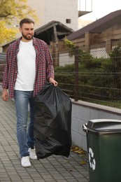 Photo of Man carrying garbage bag to recycling bin outdoors