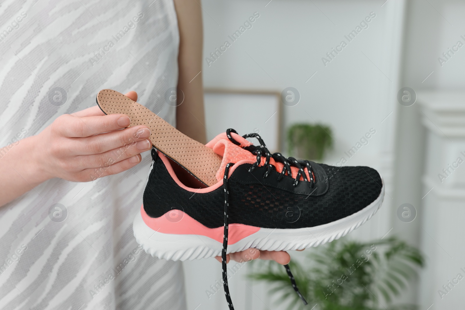 Photo of Woman putting orthopedic insole into shoe indoors, closeup. Foot care