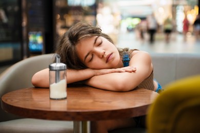 Tired teenage girl sleeping on wooden table in cafe