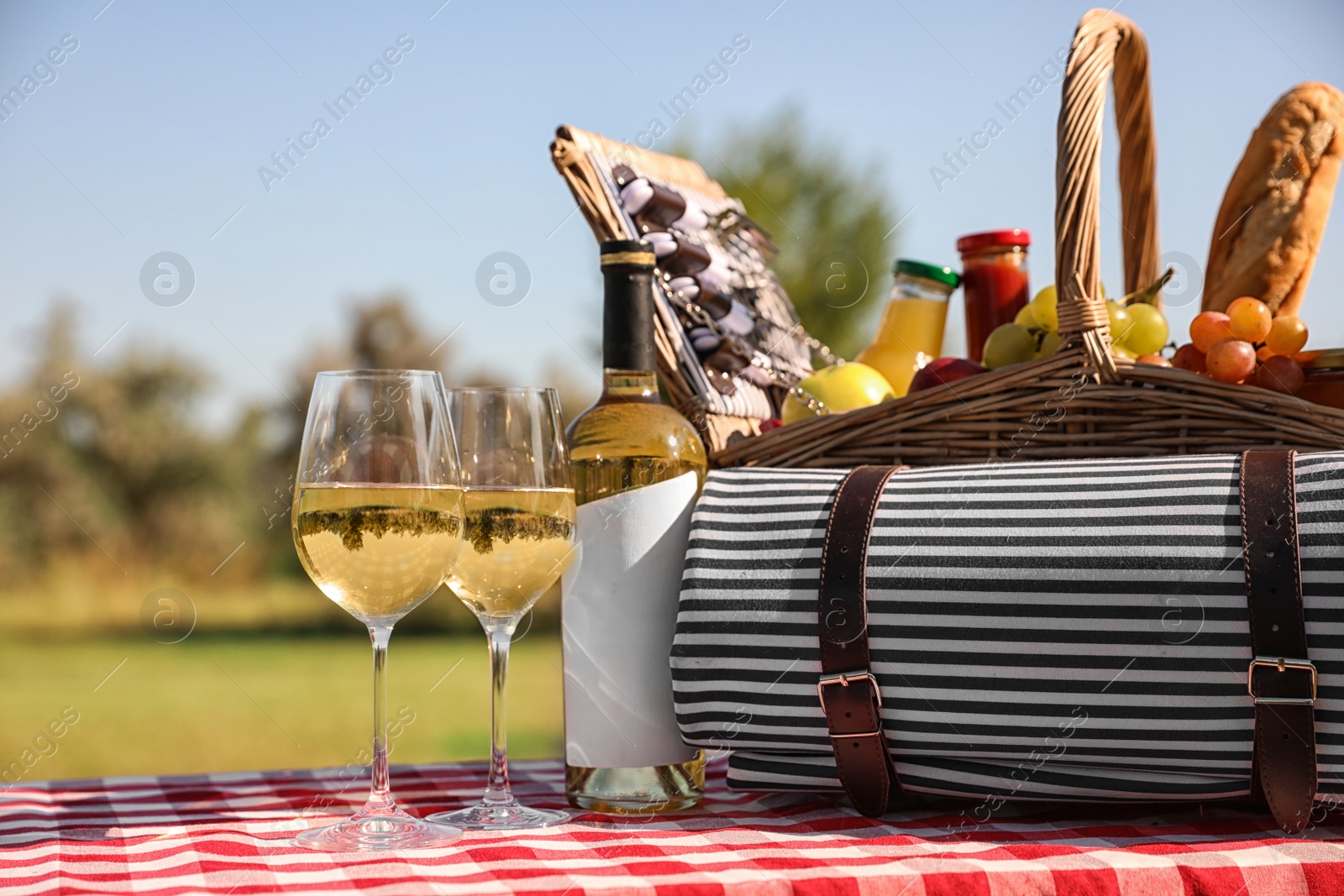 Photo of Picnic basket with wine, snacks and mat on table in park